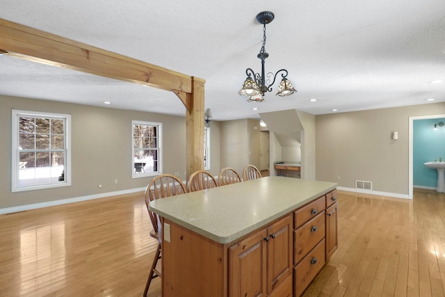 kitchen with hanging light fixtures, light wood-type flooring, a center island, brown cabinetry, and a kitchen bar