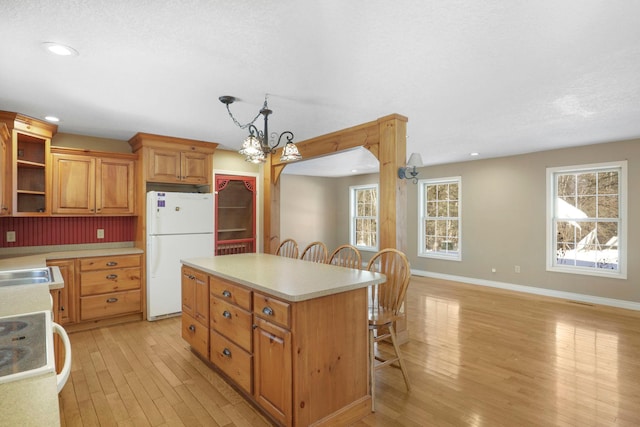 kitchen with hanging light fixtures, light countertops, freestanding refrigerator, and brown cabinets