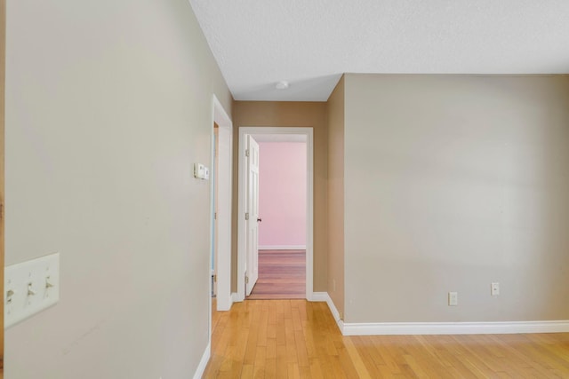 hallway featuring light wood-style floors, a textured ceiling, and baseboards