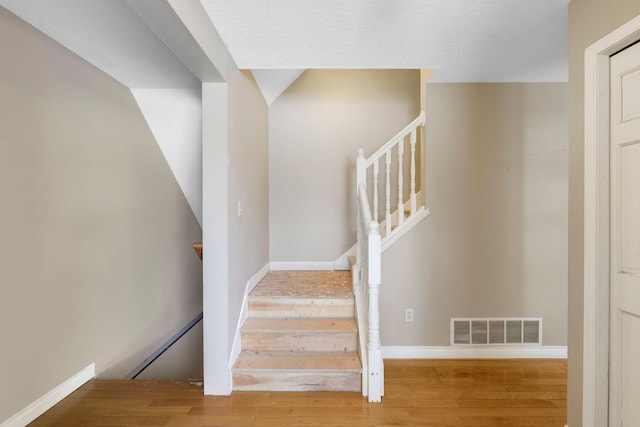 stairway featuring wood finished floors, visible vents, and baseboards