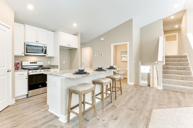 kitchen with a center island, a kitchen bar, appliances with stainless steel finishes, white cabinetry, and light stone counters