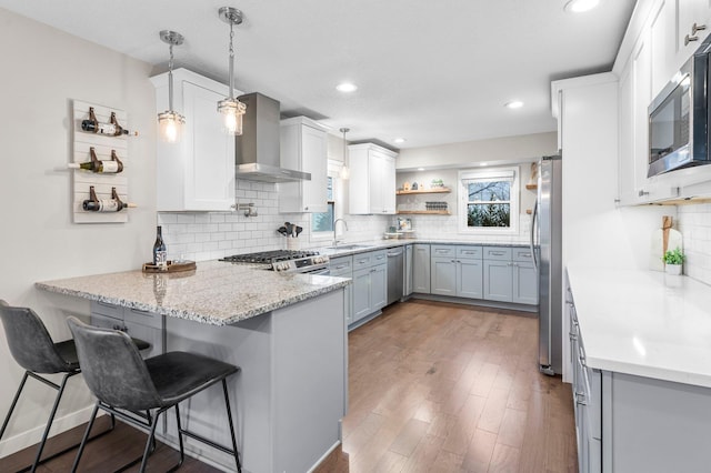 kitchen featuring wall chimney range hood, decorative light fixtures, white cabinets, sink, and kitchen peninsula