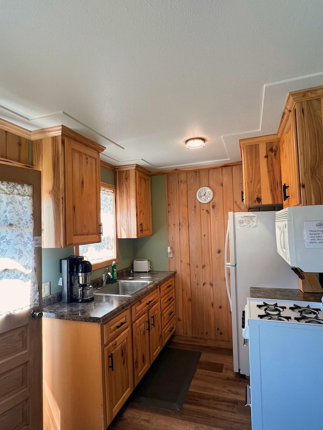 kitchen with dark wood-type flooring, sink, wood walls, a textured ceiling, and white appliances