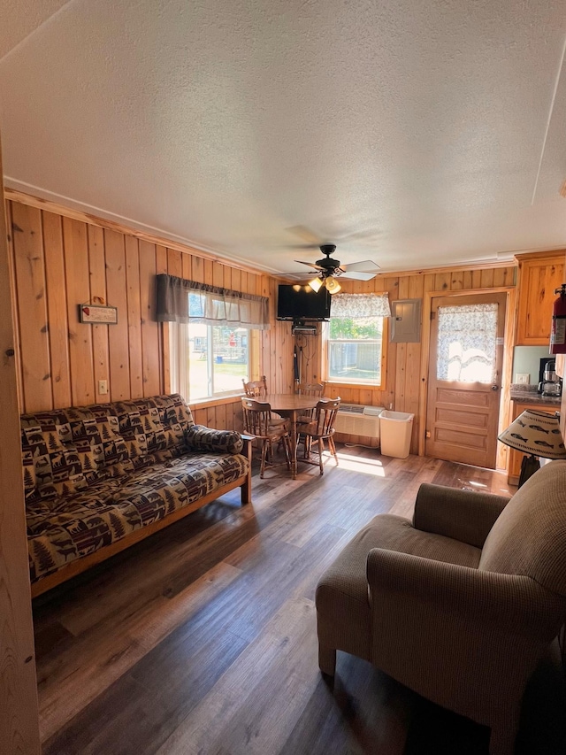 living room featuring wooden walls, hardwood / wood-style flooring, ornamental molding, ceiling fan, and a textured ceiling