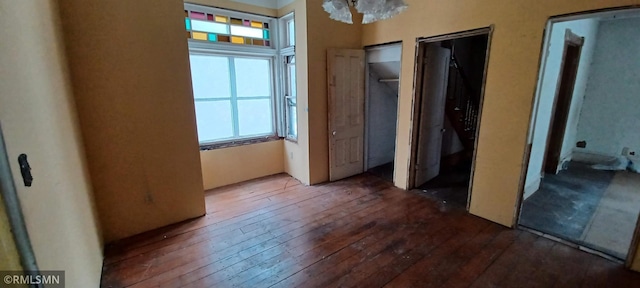 unfurnished bedroom featuring dark hardwood / wood-style flooring, a notable chandelier, and two closets