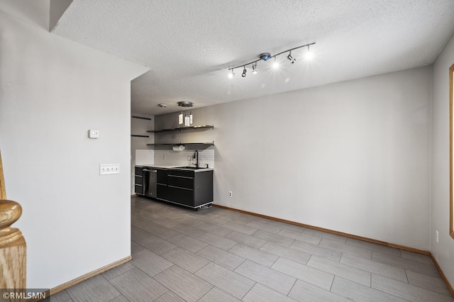 interior space featuring tasteful backsplash, sink, rail lighting, and a textured ceiling