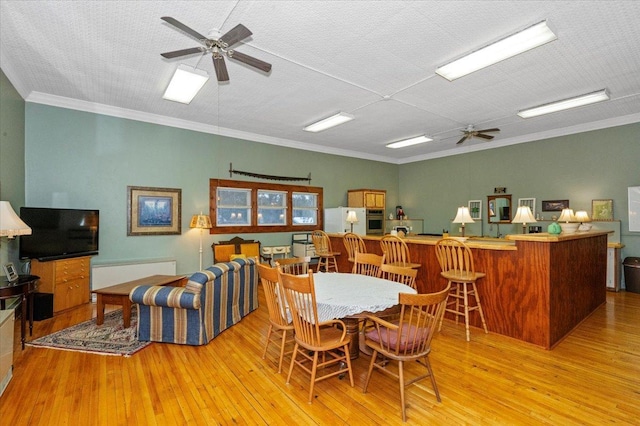 dining area featuring crown molding, indoor bar, light hardwood / wood-style flooring, and ceiling fan