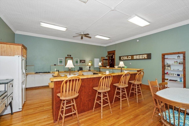 kitchen with white fridge with ice dispenser, light hardwood / wood-style flooring, crown molding, and a breakfast bar