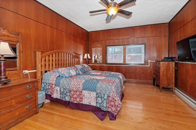 bedroom with ceiling fan, a baseboard heating unit, light hardwood / wood-style flooring, and wood walls