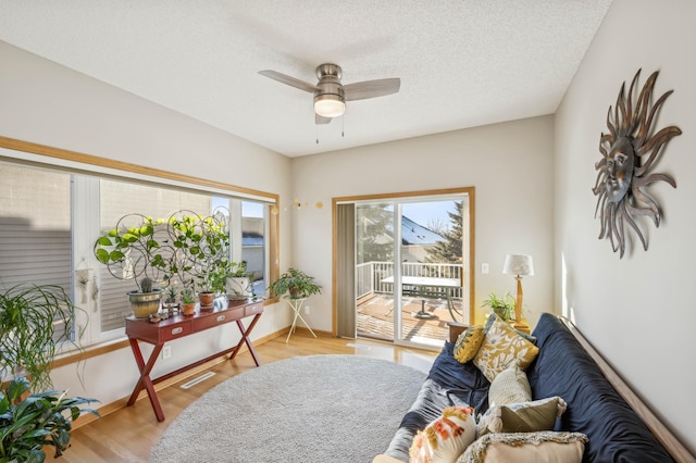 living area with ceiling fan, a textured ceiling, and light wood-type flooring