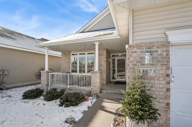 snow covered property entrance featuring a porch and a garage