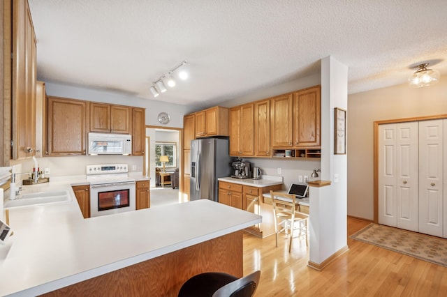 kitchen with sink, white appliances, a textured ceiling, kitchen peninsula, and light wood-type flooring