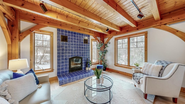 living room with a tiled fireplace, light hardwood / wood-style flooring, wooden ceiling, and beamed ceiling