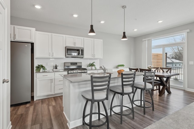 kitchen with white cabinetry, appliances with stainless steel finishes, an island with sink, and decorative light fixtures