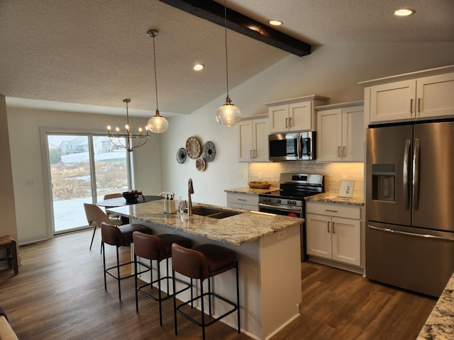 kitchen with sink, appliances with stainless steel finishes, white cabinetry, backsplash, and a center island with sink