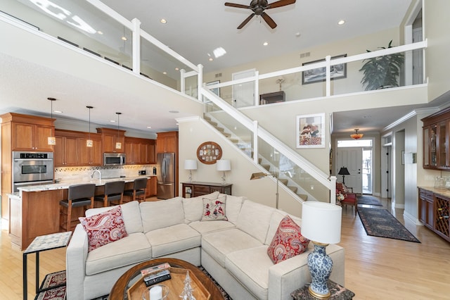 living room with visible vents, light wood-style flooring, ornamental molding, stairs, and a high ceiling