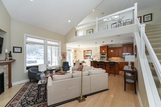 living area with light wood finished floors, baseboards, stairs, a fireplace, and high vaulted ceiling