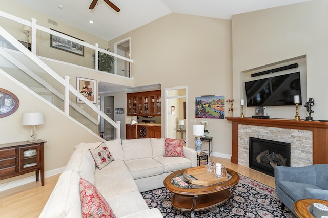 living room with a stone fireplace, wood finished floors, visible vents, a ceiling fan, and stairway