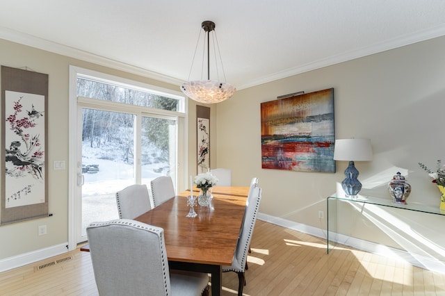 dining room with light wood-style floors, visible vents, crown molding, and baseboards