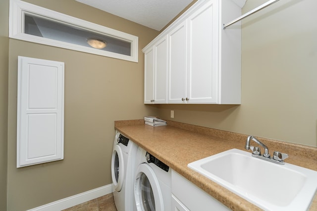 laundry room with cabinet space, baseboards, a textured ceiling, washer and dryer, and a sink