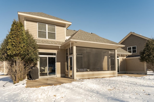 snow covered house with a sunroom and a shingled roof