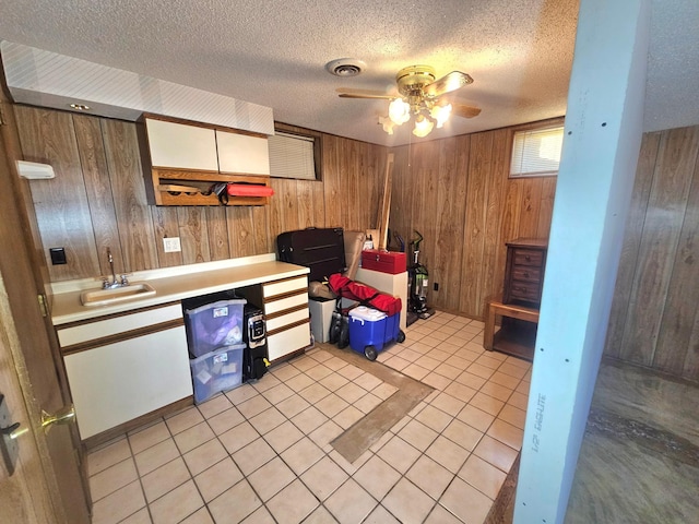 kitchen featuring sink, light tile patterned floors, ceiling fan, a textured ceiling, and wood walls