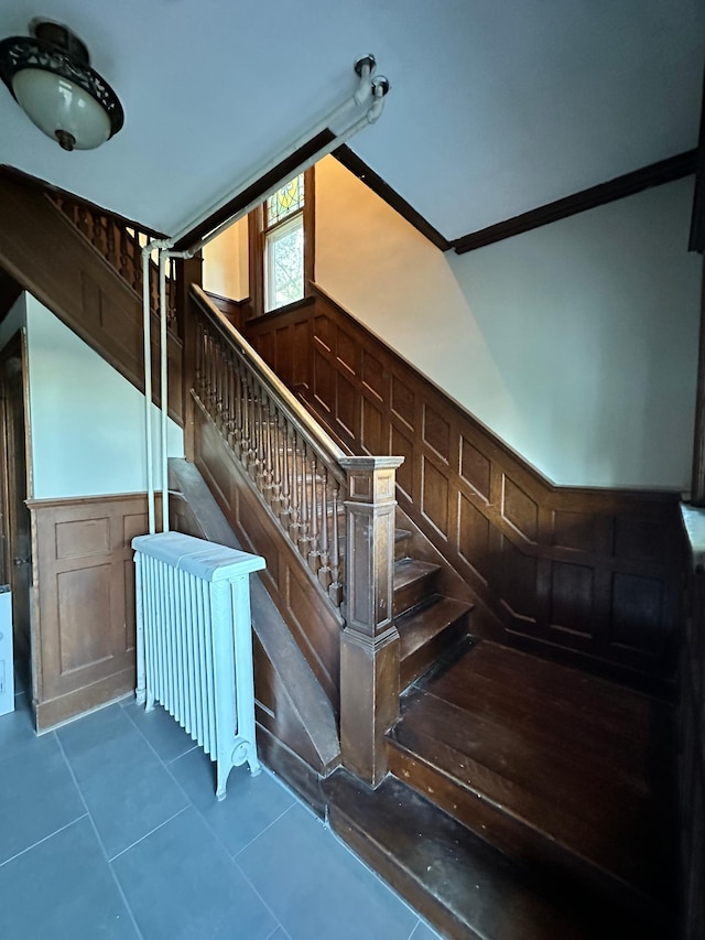 staircase with crown molding, wooden walls, and tile patterned floors