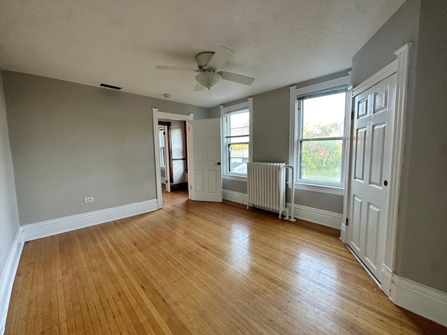 unfurnished bedroom with ceiling fan, radiator heating unit, light hardwood / wood-style flooring, and a textured ceiling