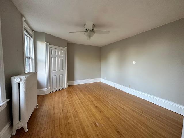 empty room with ceiling fan, radiator heating unit, light hardwood / wood-style flooring, and a textured ceiling