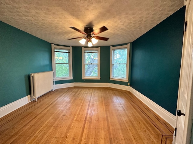 empty room with ceiling fan, radiator, a textured ceiling, and light hardwood / wood-style flooring