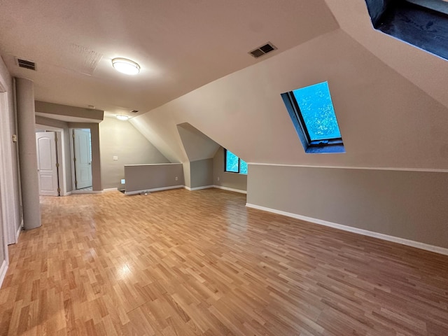 additional living space with vaulted ceiling with skylight and light hardwood / wood-style flooring