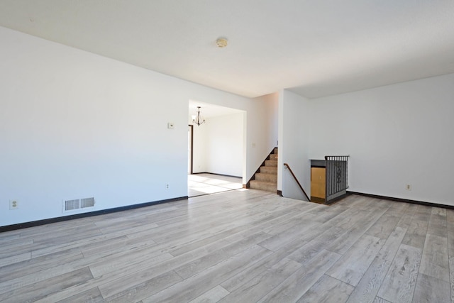 unfurnished room featuring a notable chandelier and light wood-type flooring