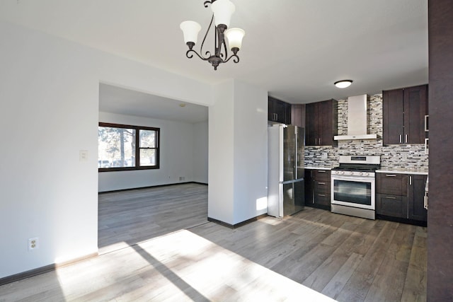 kitchen featuring appliances with stainless steel finishes, decorative backsplash, hanging light fixtures, dark brown cabinets, and wall chimney range hood