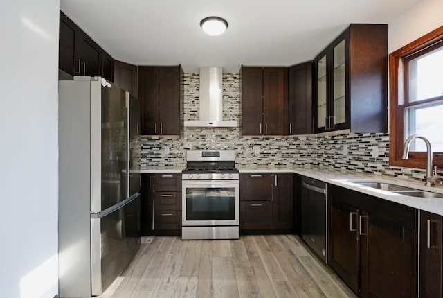 kitchen featuring wall chimney exhaust hood, sink, light hardwood / wood-style flooring, appliances with stainless steel finishes, and decorative backsplash