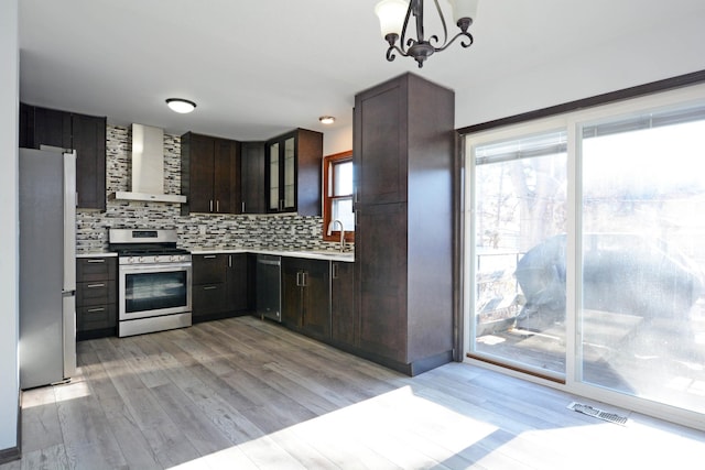 kitchen with sink, backsplash, stainless steel appliances, light wood-type flooring, and wall chimney exhaust hood