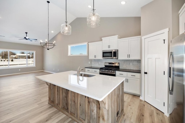 kitchen featuring sink, white cabinetry, decorative light fixtures, appliances with stainless steel finishes, and an island with sink