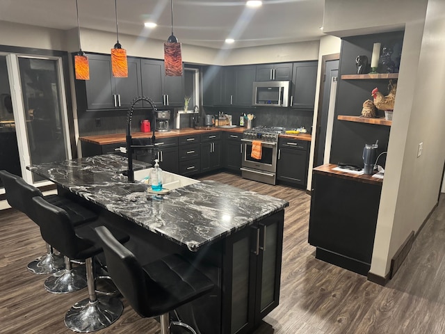 kitchen with appliances with stainless steel finishes, hanging light fixtures, a kitchen breakfast bar, sink, and dark stone counters