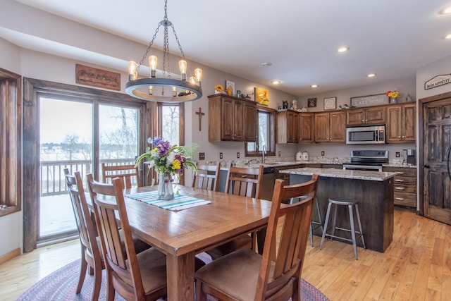 dining space with an inviting chandelier, sink, and light hardwood / wood-style flooring