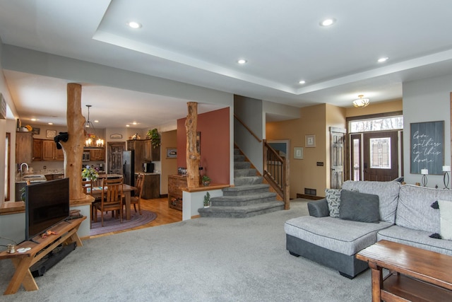 living room with an inviting chandelier, light colored carpet, a raised ceiling, and sink