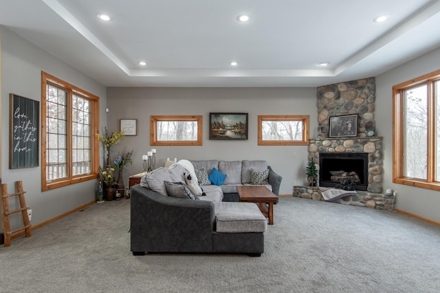 living room featuring a stone fireplace, light colored carpet, and a tray ceiling