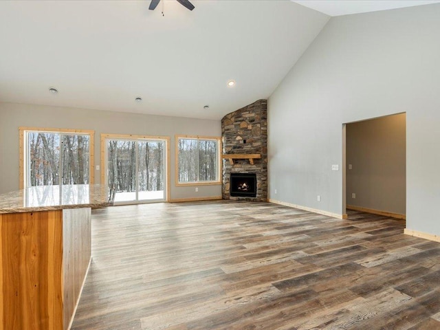 unfurnished living room with hardwood / wood-style flooring, a stone fireplace, high vaulted ceiling, and ceiling fan