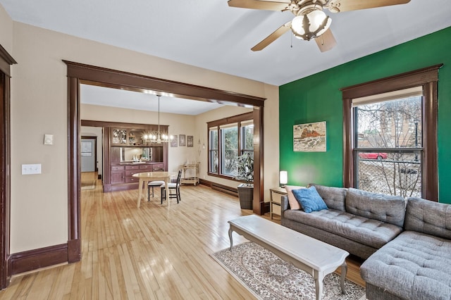 living room with light hardwood / wood-style flooring, ceiling fan with notable chandelier, and plenty of natural light