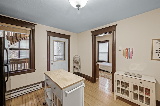 kitchen with baseboard heating, black fridge, light hardwood / wood-style floors, and a textured ceiling