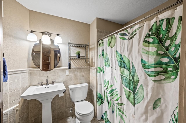 bathroom with tile walls, toilet, a textured ceiling, and walk in shower