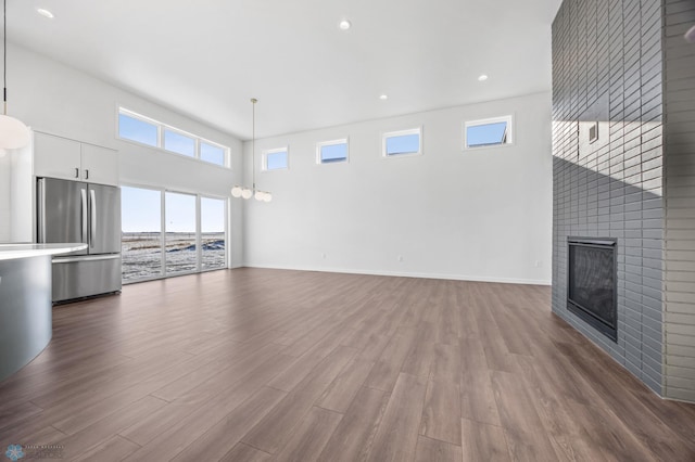 unfurnished living room featuring a high ceiling, wood-type flooring, a large fireplace, and a chandelier