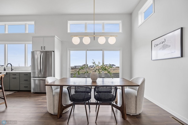 dining space with baseboards, visible vents, dark wood-style floors, and a towering ceiling