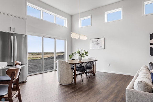 dining room with dark wood-style flooring, baseboards, and a towering ceiling