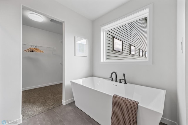full bath with baseboards, tile patterned flooring, a walk in closet, and a freestanding tub