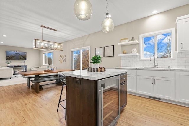 kitchen featuring light wood finished floors, beverage cooler, backsplash, and a sink