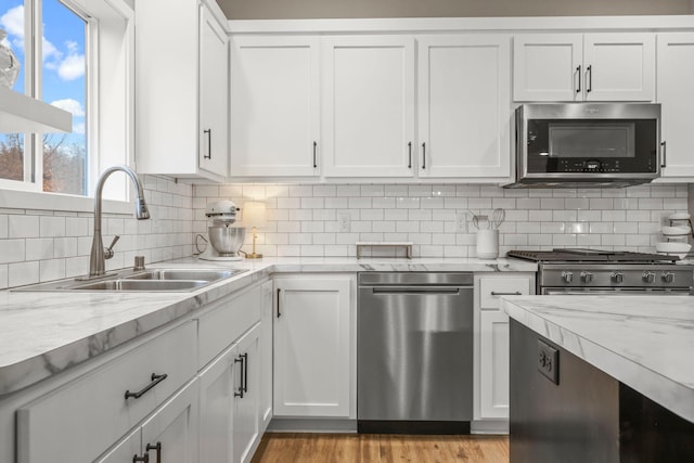 kitchen with appliances with stainless steel finishes, a sink, white cabinetry, and tasteful backsplash